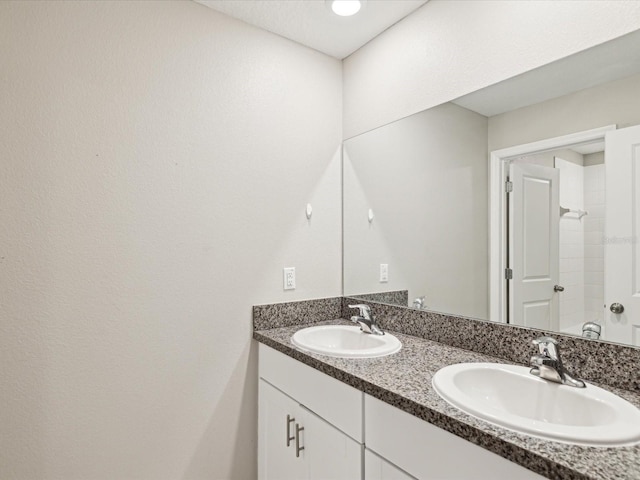 full bathroom with double vanity, a shower, and a sink