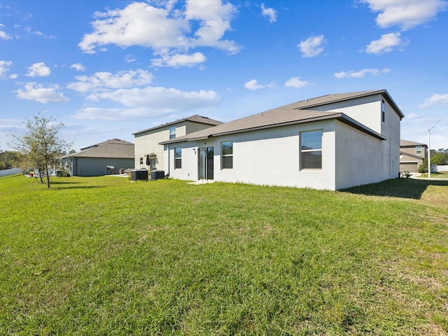 rear view of house with a lawn, central AC, and stucco siding