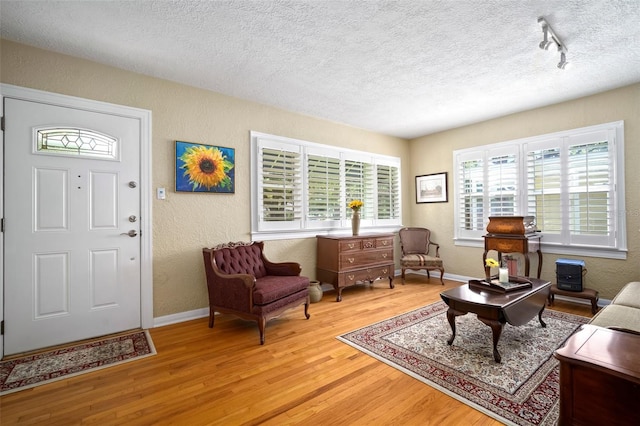 living room with track lighting, a textured ceiling, wood finished floors, baseboards, and a textured wall