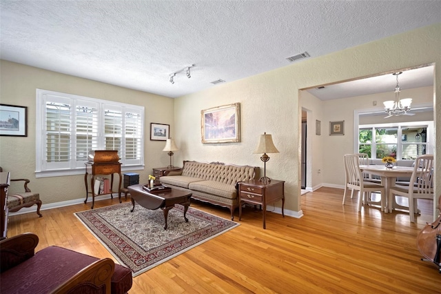 living room featuring visible vents, plenty of natural light, an inviting chandelier, and hardwood / wood-style flooring