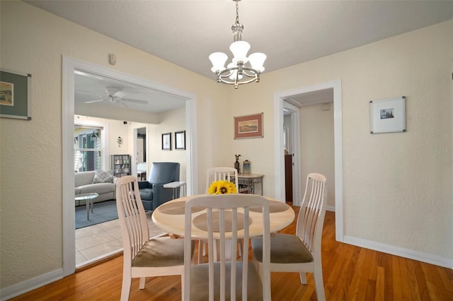 dining area featuring ceiling fan with notable chandelier, baseboards, light wood-type flooring, and a textured wall