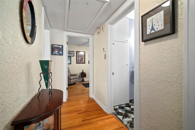 hallway featuring attic access, wood finished floors, and a textured wall