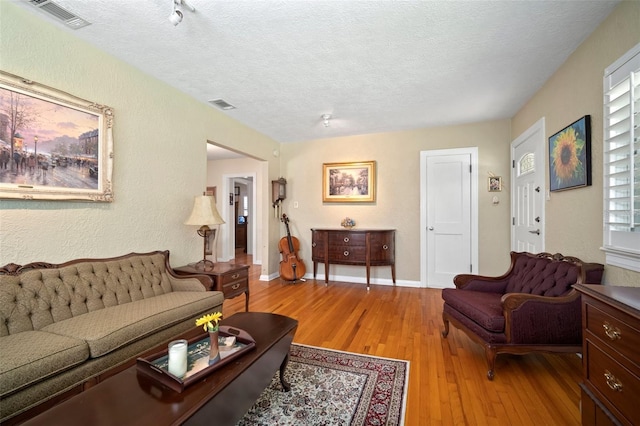 living area featuring a textured wall, visible vents, light wood finished floors, and a textured ceiling