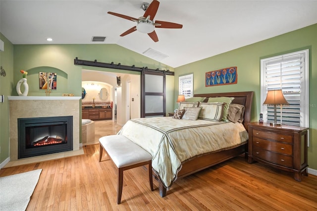 bedroom featuring wood finished floors, visible vents, a sink, vaulted ceiling, and a barn door