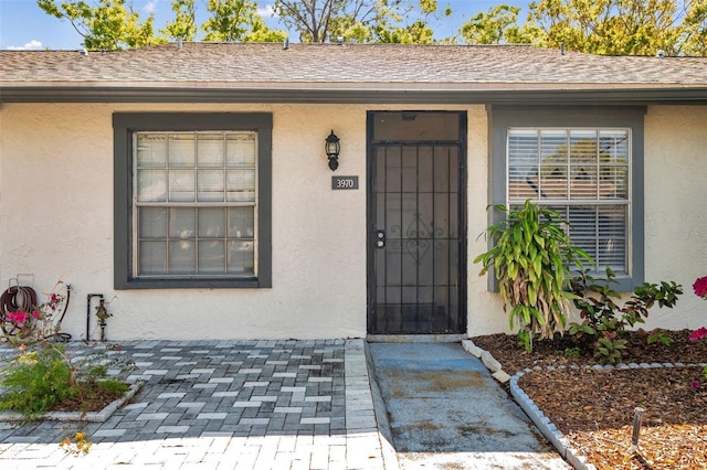 property entrance featuring a shingled roof and stucco siding