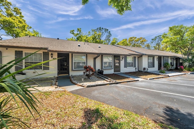 single story home with uncovered parking, roof with shingles, and stucco siding