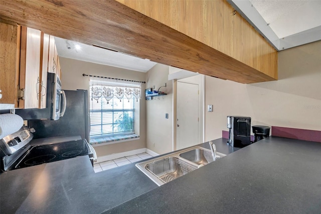 kitchen with a sink, dark countertops, appliances with stainless steel finishes, light tile patterned floors, and baseboards