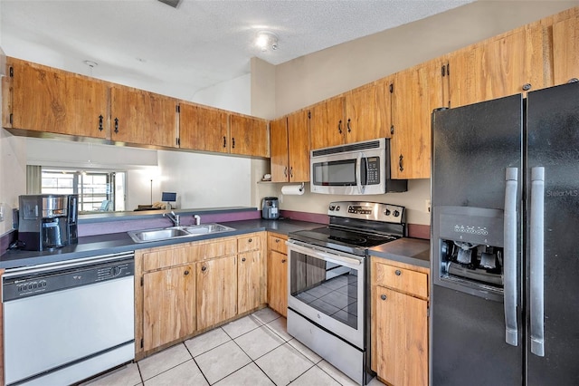 kitchen featuring light tile patterned floors, a sink, appliances with stainless steel finishes, a textured ceiling, and dark countertops