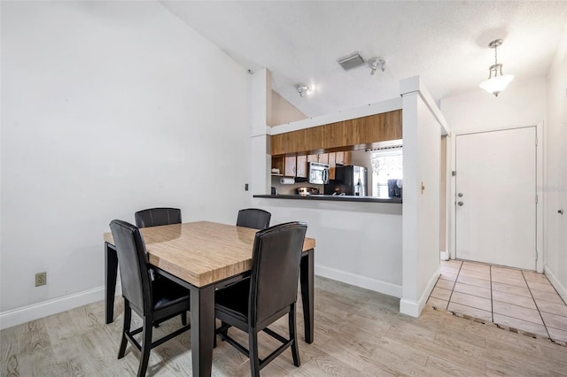 dining room with vaulted ceiling, visible vents, baseboards, and light wood finished floors