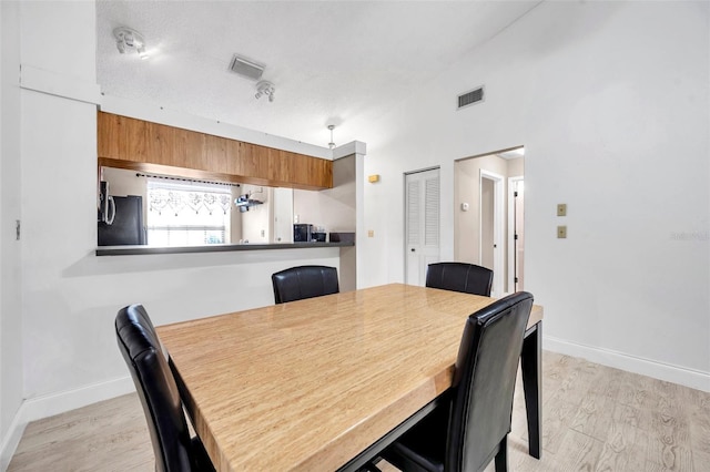 dining space featuring visible vents, baseboards, light wood-style floors, and vaulted ceiling