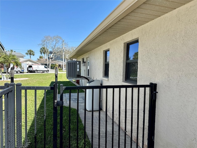 view of side of home featuring central air condition unit, stucco siding, a yard, and fence