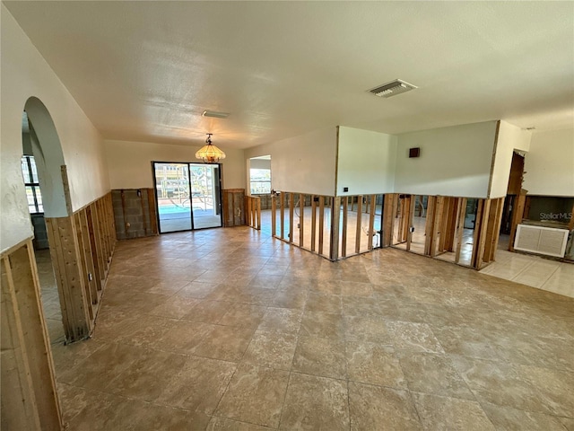 unfurnished room with visible vents, a wainscoted wall, and arched walkways