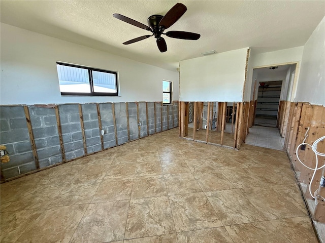 empty room with visible vents, a textured ceiling, ceiling fan, and wainscoting