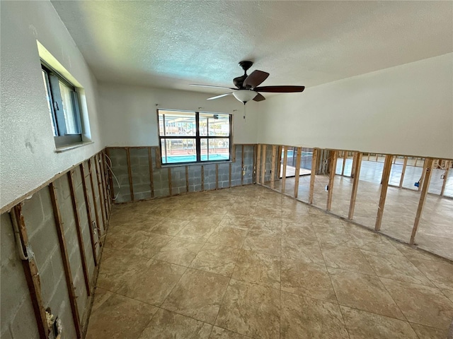 spare room featuring wainscoting, a textured ceiling, tile walls, and a ceiling fan