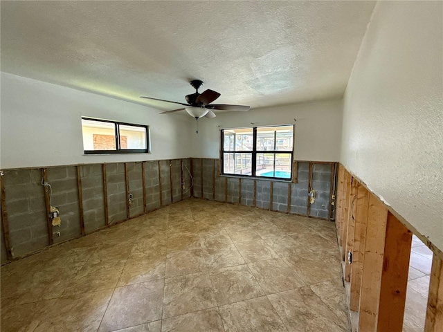 spare room featuring a ceiling fan, a textured ceiling, and wainscoting