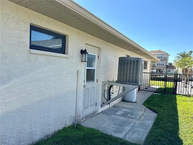 doorway to property featuring stucco siding, central air condition unit, a yard, and fence