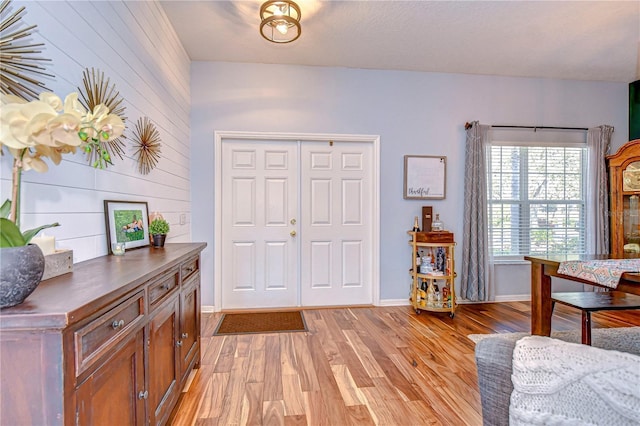 entrance foyer with light wood-type flooring, baseboards, and wooden walls