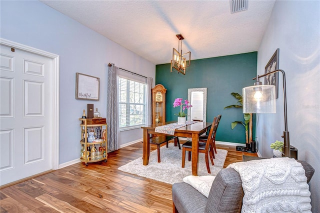 dining space with visible vents, baseboards, a chandelier, wood finished floors, and a textured ceiling