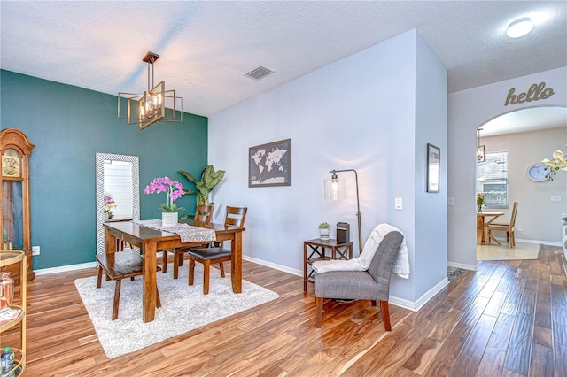 dining area featuring visible vents, baseboards, an inviting chandelier, wood finished floors, and arched walkways