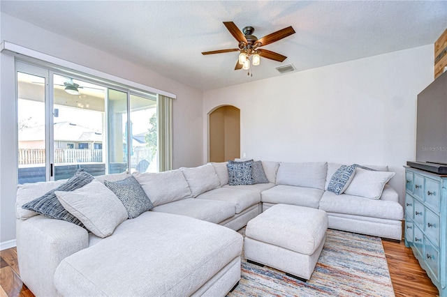 living room featuring arched walkways, a ceiling fan, visible vents, and light wood-type flooring