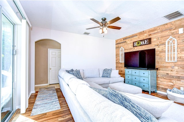 living area featuring arched walkways, visible vents, wood walls, and wood finished floors