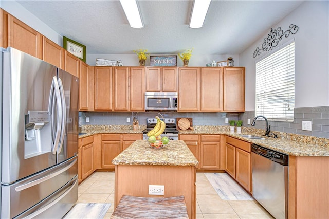 kitchen featuring light stone countertops, light tile patterned flooring, a sink, appliances with stainless steel finishes, and a center island