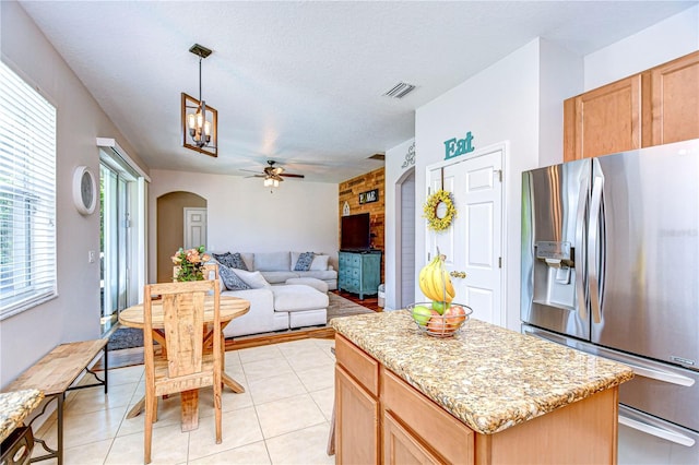 kitchen featuring visible vents, a kitchen island, arched walkways, decorative light fixtures, and stainless steel fridge