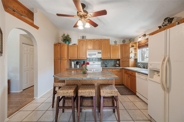 kitchen featuring visible vents, a kitchen bar, a sink, white appliances, and vaulted ceiling