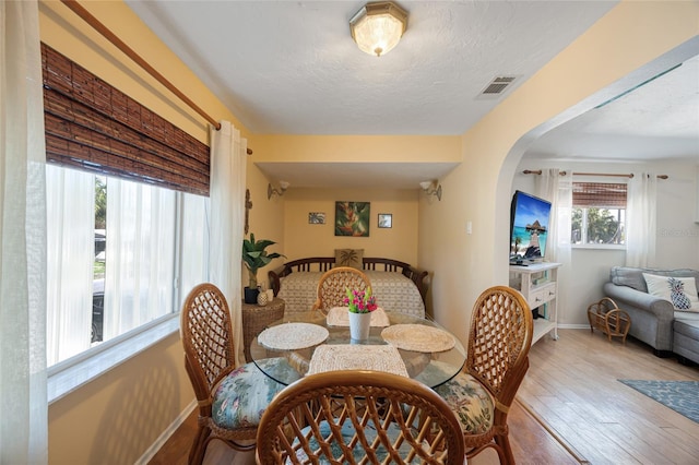 dining space featuring hardwood / wood-style floors, visible vents, baseboards, arched walkways, and a textured ceiling