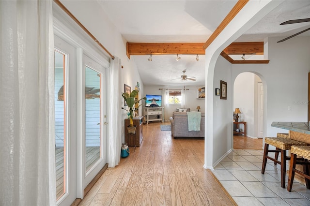 hall with arched walkways, beamed ceiling, light wood finished floors, and baseboards