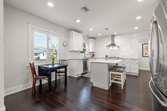 kitchen featuring wall chimney range hood, backsplash, appliances with stainless steel finishes, and visible vents