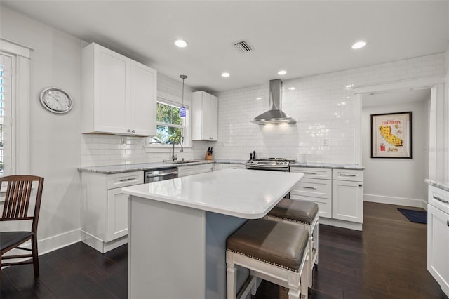 kitchen featuring wall chimney range hood, appliances with stainless steel finishes, a sink, baseboards, and dark wood-type flooring