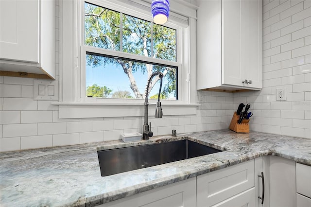 kitchen featuring a sink, decorative backsplash, light stone countertops, and white cabinetry
