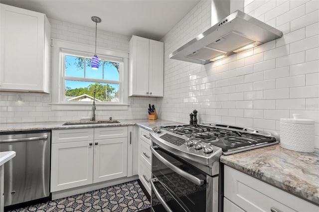 kitchen with wall chimney range hood, decorative backsplash, appliances with stainless steel finishes, a sink, and white cabinetry