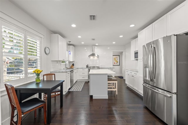 kitchen featuring wall chimney range hood, decorative backsplash, visible vents, appliances with stainless steel finishes, and a center island