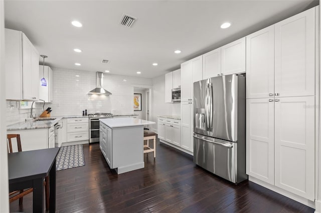 kitchen with wall chimney range hood, appliances with stainless steel finishes, a sink, tasteful backsplash, and visible vents