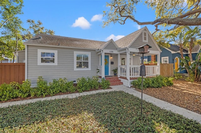 bungalow-style home featuring a porch, fence, and a shingled roof