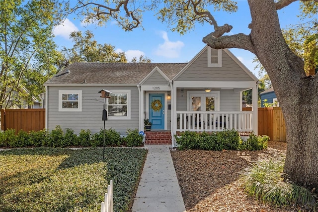 bungalow-style home with a porch, roof with shingles, and fence