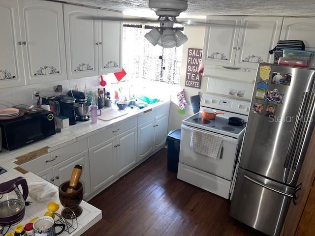 kitchen with dark wood-type flooring, black microwave, freestanding refrigerator, electric range, and white cabinetry