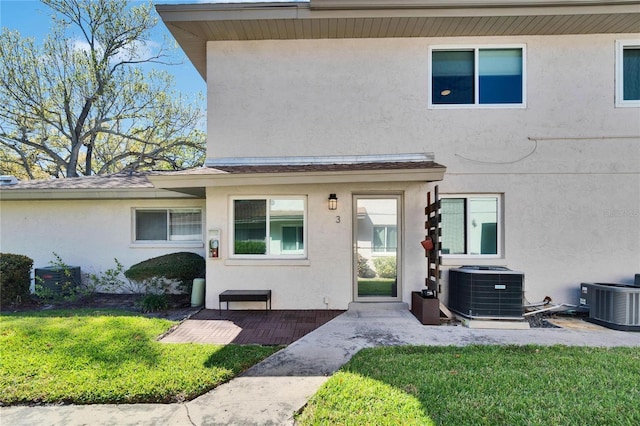 view of front of home with stucco siding, central AC, and a front yard