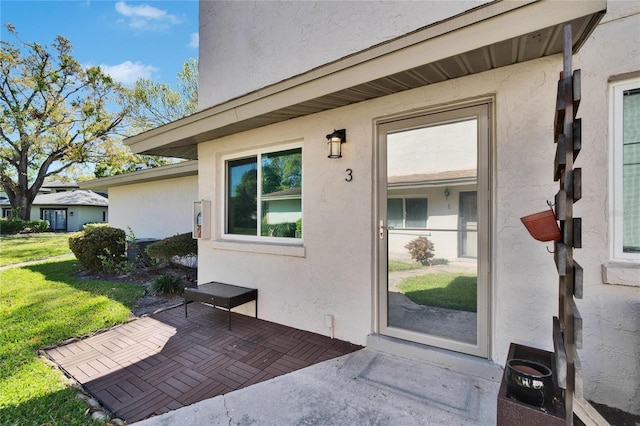 property entrance featuring stucco siding, a patio, and a lawn