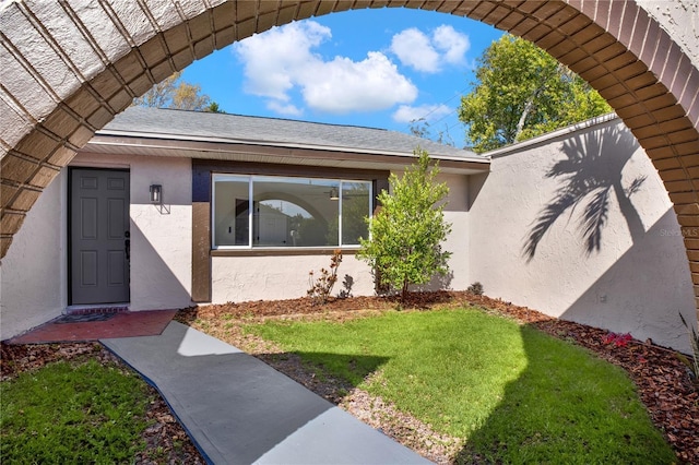 property entrance with a shingled roof, a yard, and stucco siding