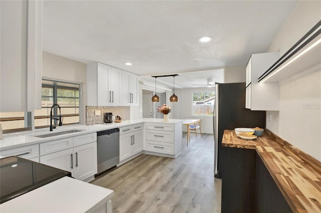 kitchen featuring a peninsula, a sink, appliances with stainless steel finishes, wood counters, and white cabinetry