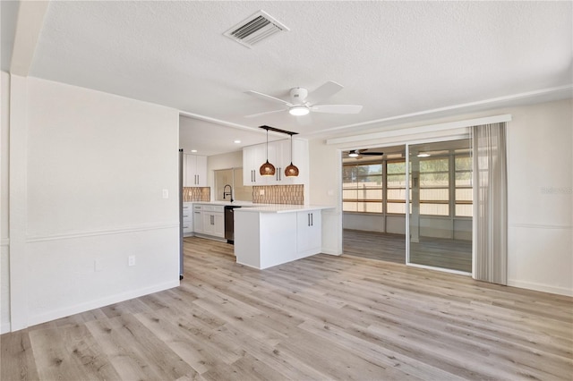 kitchen featuring visible vents, a peninsula, light wood-style flooring, light countertops, and dishwasher