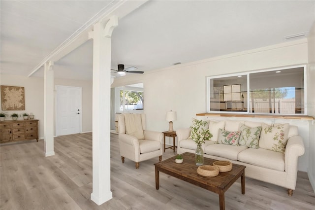 living room with visible vents, light wood-style floors, crown molding, ceiling fan, and ornate columns