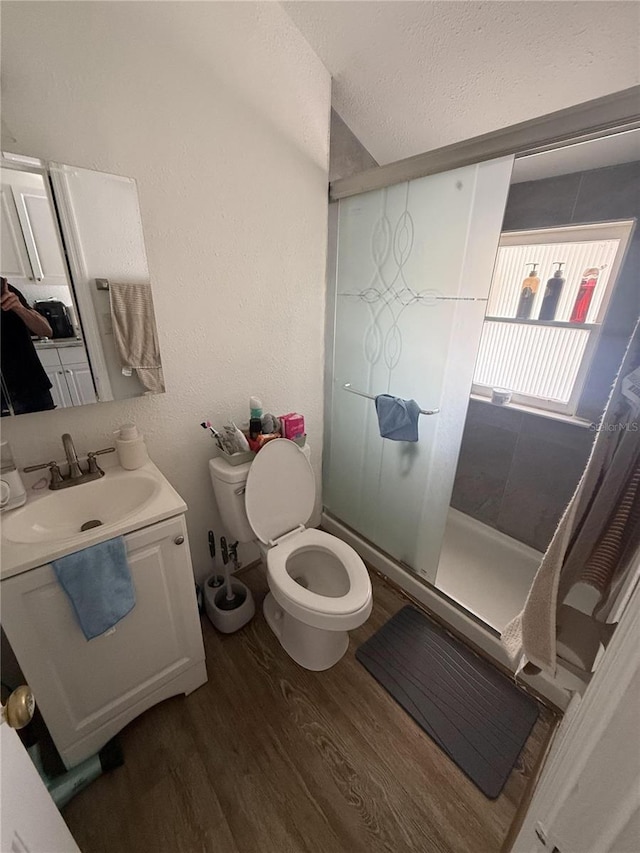 full bathroom featuring vanity, wood finished floors, a shower stall, a textured ceiling, and toilet