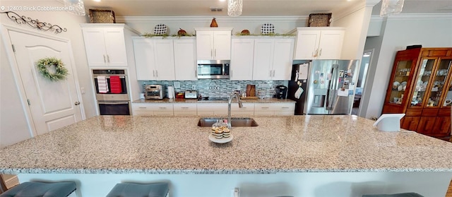 kitchen with backsplash, ornamental molding, a large island with sink, stainless steel appliances, and a sink