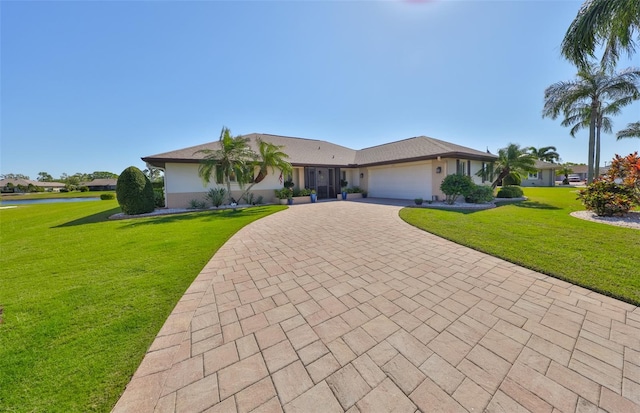 ranch-style house featuring a front yard, decorative driveway, an attached garage, and stucco siding