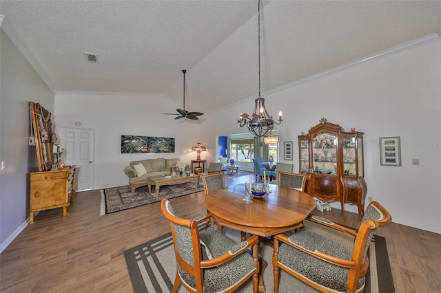 dining room featuring wood finished floors, visible vents, lofted ceiling, ornamental molding, and a textured ceiling