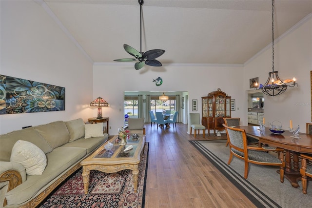 living area with ceiling fan with notable chandelier, ornamental molding, wood finished floors, and high vaulted ceiling